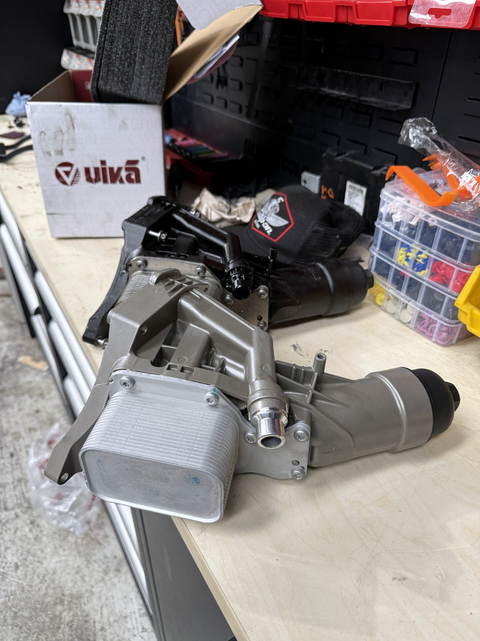 Original plastic oil filter housing and replacement assembly on the Luca Motors workshop bench